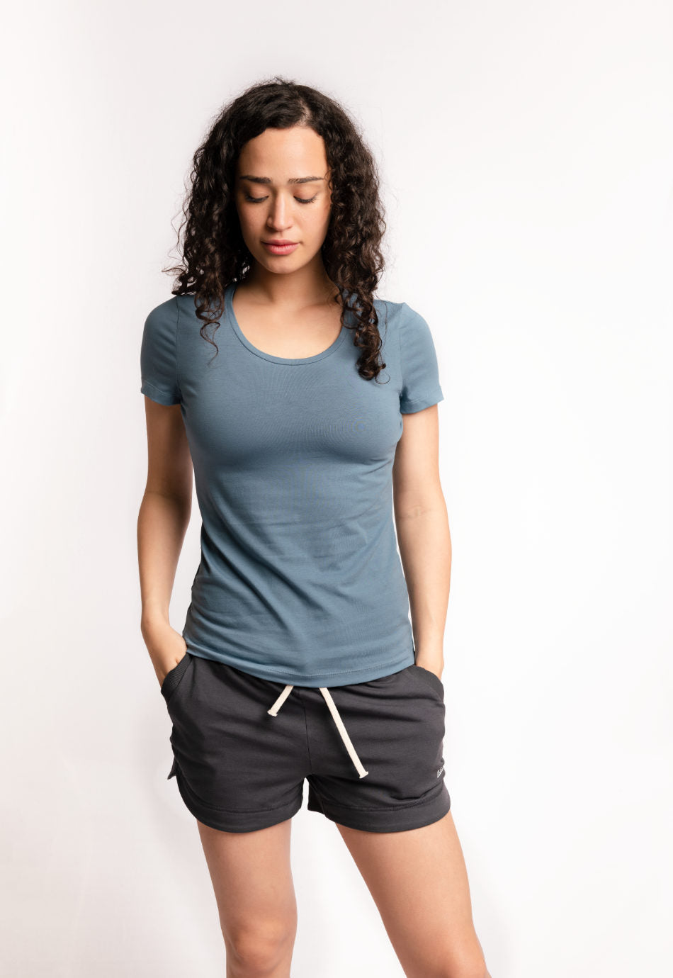 Frau traegt das M23 „Lola“ T-Shirt in gedecktem Blau aus weicher, nachhaltiger Bio-Baumwolle – minimalistisches, umweltfreundliches Design.