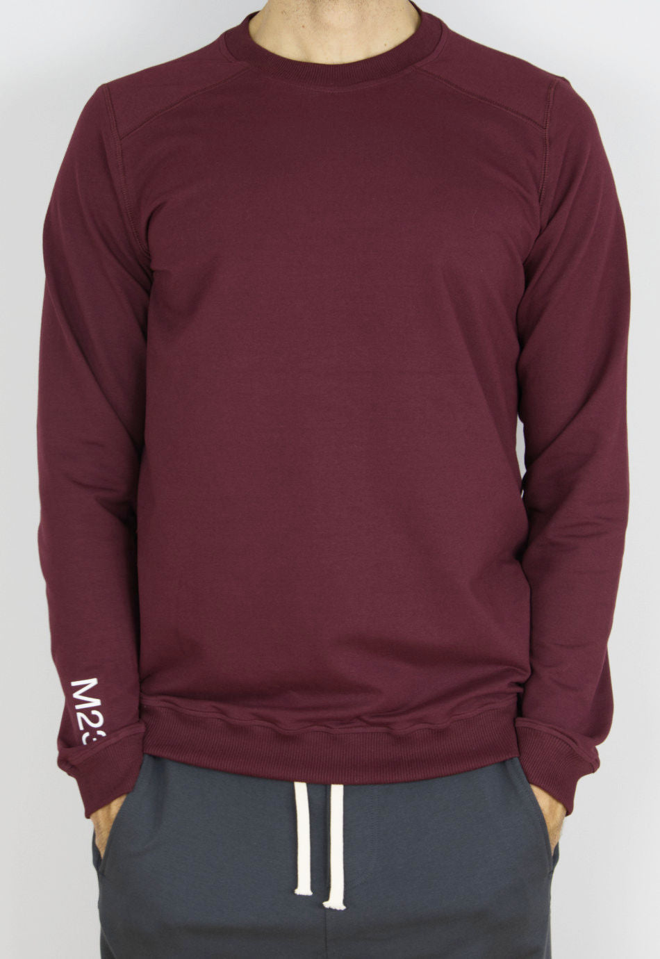 Mann traegt das M23 Sweatshirt „Phil“ in Bordeauxrot aus nachhaltiger Bio-Baumwolle mit M23-Print am Aermel – faire und umweltfreundliche Herrenmode.