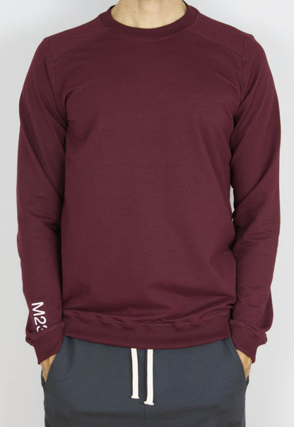 Mann traegt das M23 Sweatshirt „Phil“ in Bordeauxrot aus nachhaltiger Bio-Baumwolle mit M23-Print am Aermel – faire und umweltfreundliche Herrenmode.

